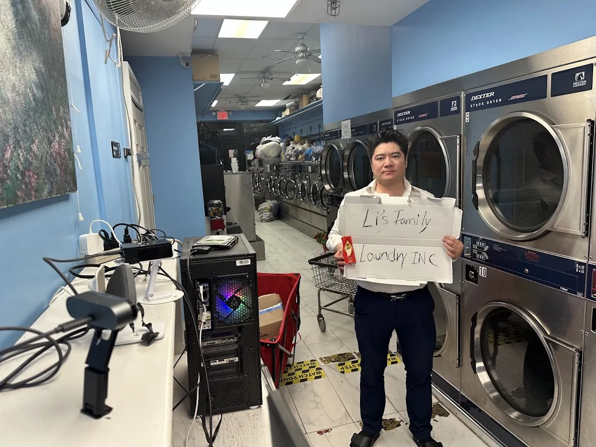 The founder holding the Li's Family Laundry sign, Pi and camera on the left, machines on the right